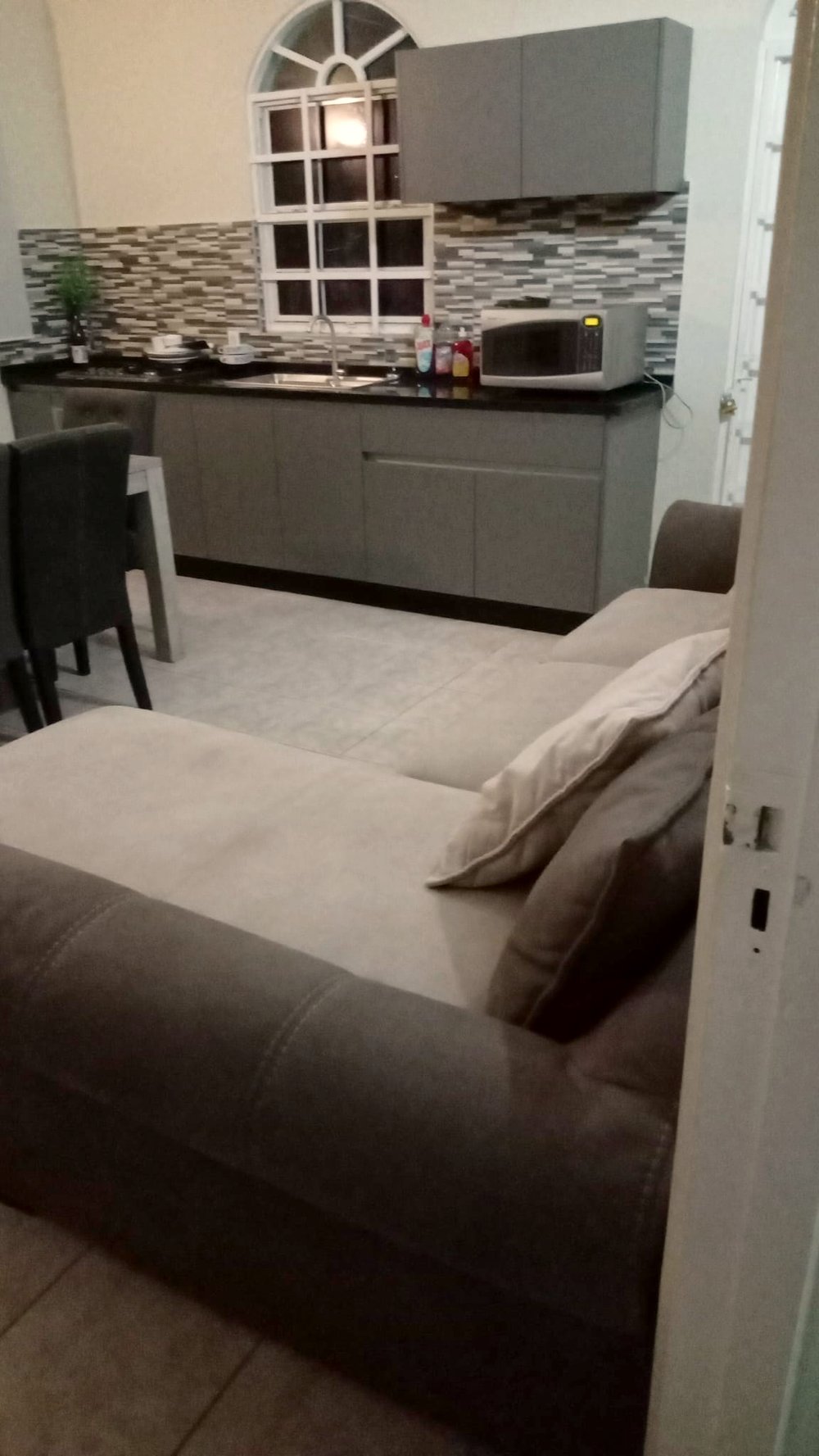 A kitchen with grey cabinets and an arched window, seen past the sofa